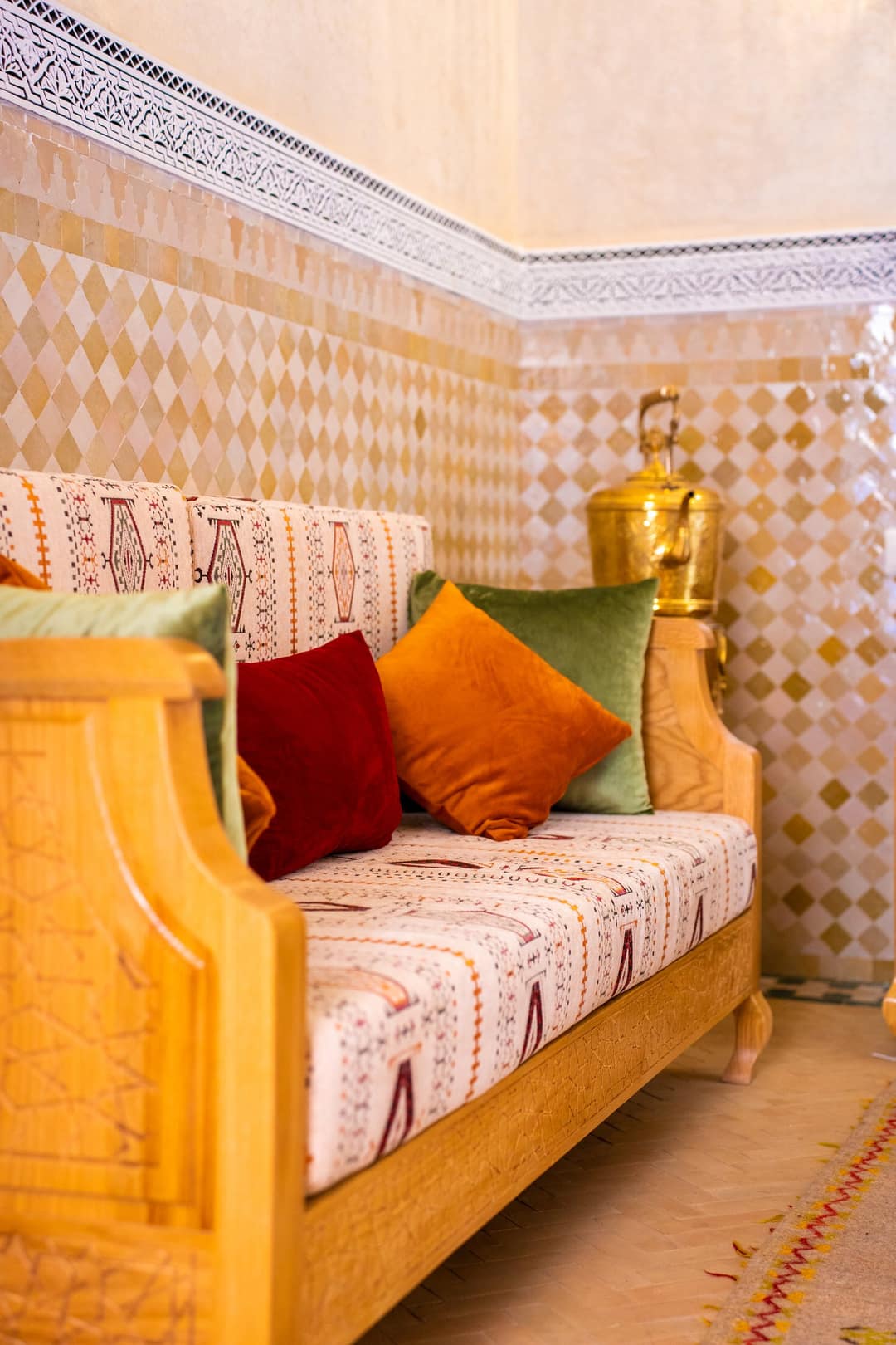 Wooden banquette with red, orange and green cushions against a zellige wall
